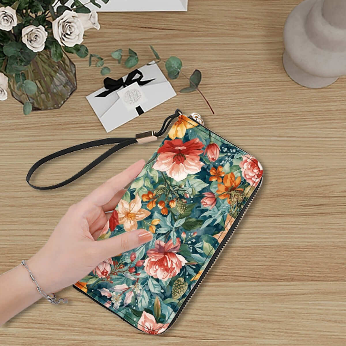 Elegante Portemonnaie mit Reißverschluss in floralem Design, gehalten von einer Hand auf einem Holztisch mit Blumenhintergrund.
