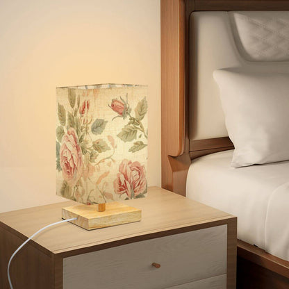 Quadratische Tischlampe aus Leinen und Gummiholz mit floralem Design auf einem Nachttisch, warmes und gemütliches Licht erzeugend.
