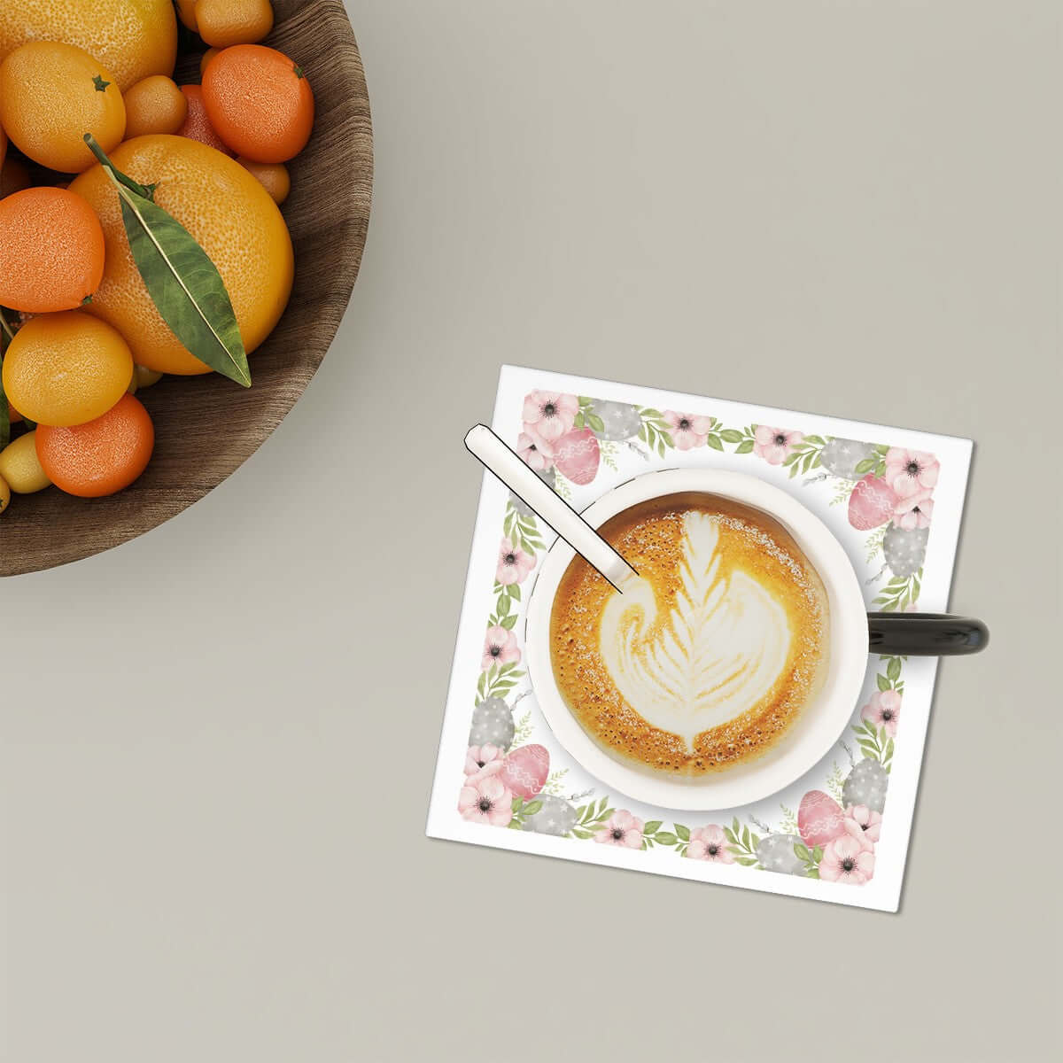 Quadratische Keramikuntersetzer, 6 Stück, mit floralem Design unter einer Kaffeetasse auf Tisch.