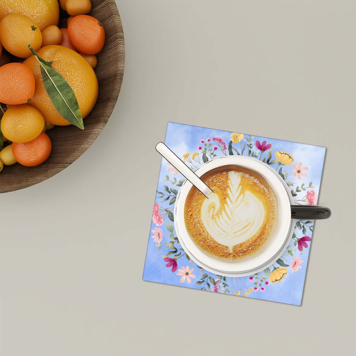 Quadratische Keramikuntersetzer, 6 Stück mit floralem Design, unter Kaffeetasse mit Latte-Art, auf Tisch neben Obstschale.